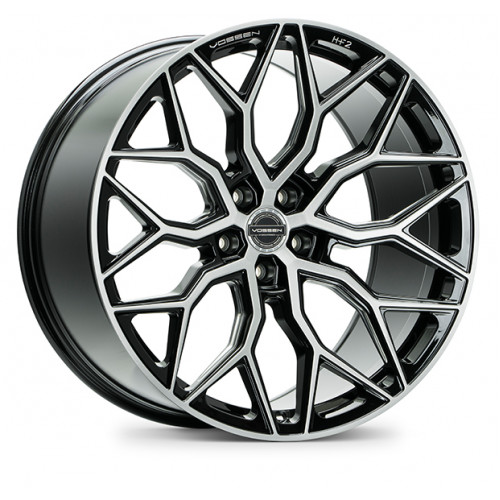 A stylish alloy wheel with an intricate, geometric spoke design in a silver and black finish is displayed against a white background. Text reads: "Vossen HF-2".