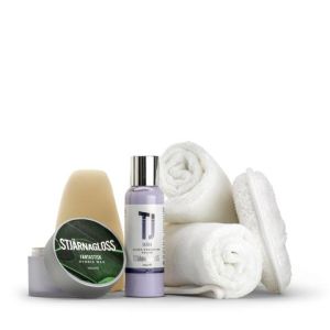Various grooming products arranged on a white surface, including a green-bottled Stjärnagloss Fantastisk Carnauba Wax, a purple TJ bottle, two rolled white towels, and a white oval scrubber.