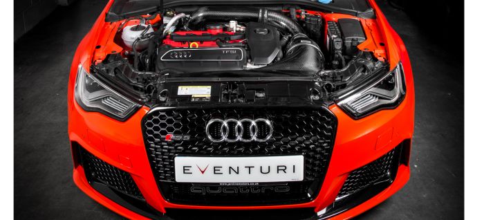 An open hood of an orange Audi RS3 reveals the engine and various components, situated in a dimly lit garage. The license plate reads "EVENTURI." The badge "quattro" appears below.