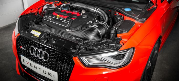 An open engine bay of an Audi car reveals a TFSI engine with Eventuri branding on the front grille in a brightly lit garage or workshop.