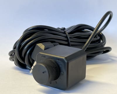 A black coiled cable with a rectangular attachment featuring a rotatable switch. Marked with "1V/5V," it lies on a light-colored surface against a light blue background.