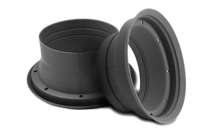 Two black cylindrical plastic flanges lay on a white surface; one flange stands upright while the other rests at an angle, partially inside the upright flange.