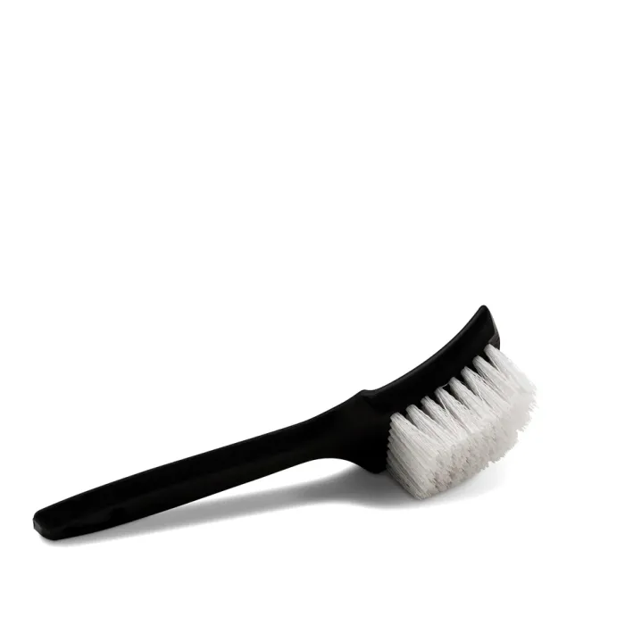 A black-handled brush with stiff, white bristles is shown lying on a plain white surface.