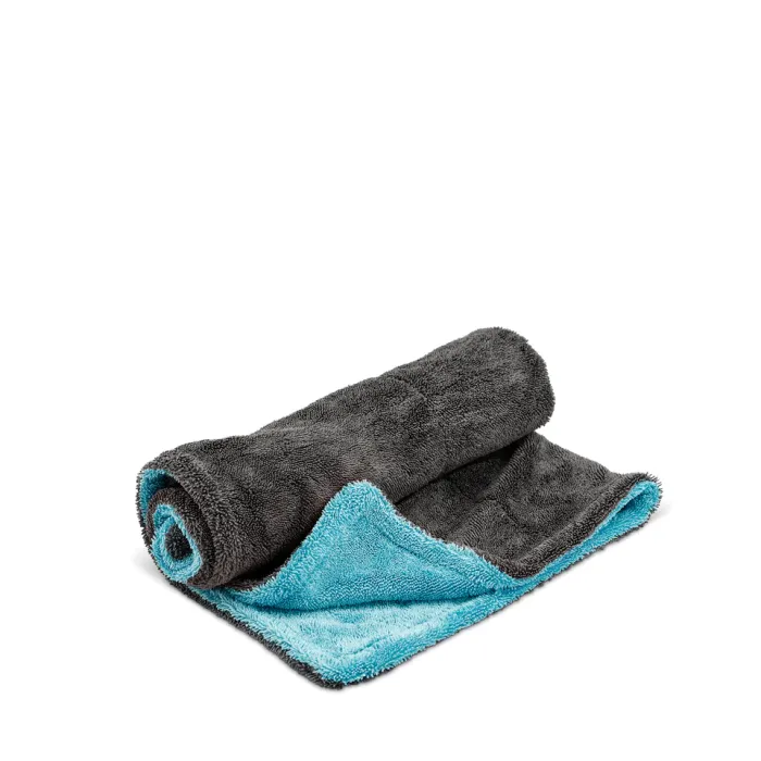A partially rolled, two-tone microfiber towel with a dark grey exterior and light blue interior rests on a plain white surface, showcasing both colors prominently.