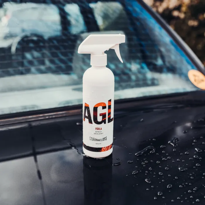 A white spray bottle labeled "AGL PÄRLA Spray Sealant STJÄRNAELOSS 500ml" standing upright on a wet car hood, with beads of water around it.