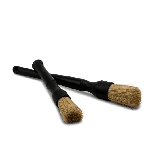 Two black-handled brushes with beige bristles lie crossed on a white background.