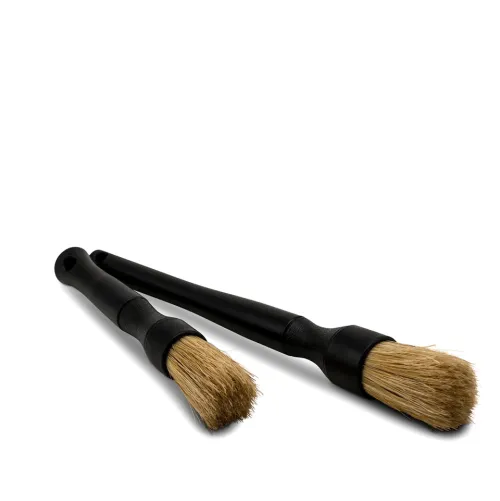 Two black-handled cleaning brushes with light brown bristles lie on a white surface, one brush positioned diagonally above the other.