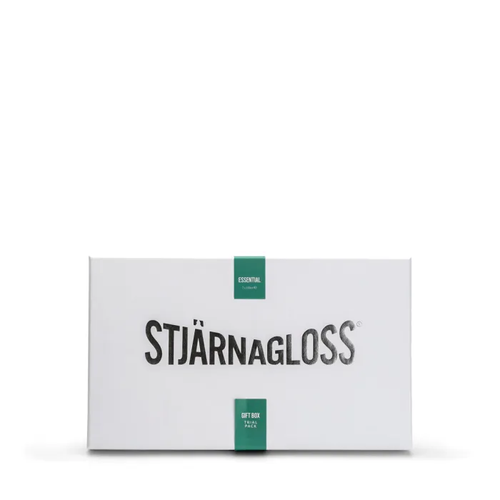 White rectangular box with black text "STJÄRNAGLOSS" and green labels reading "ESSENTIAL 7 x 100ML" and "GIFT BOX TRIAL PACK" in a plain white background.