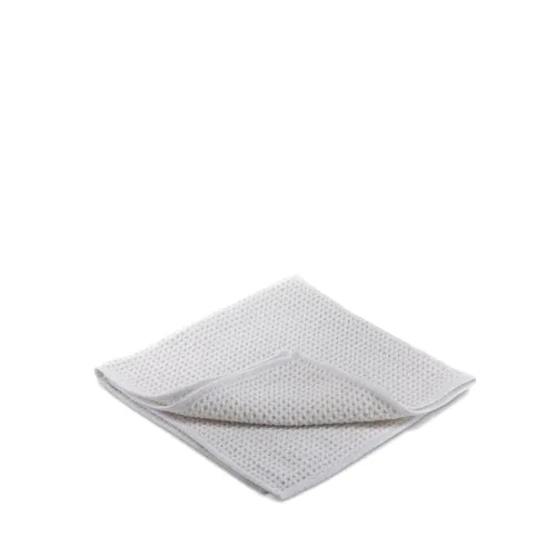 A white, textured, folded washcloth lies on a plain white background, slightly flipped at one corner to reveal its inner layer.