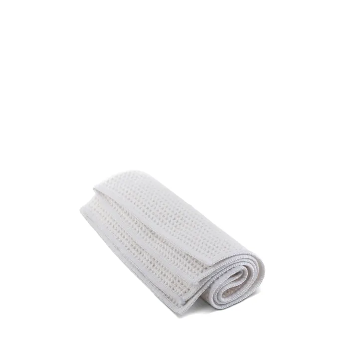 A folded white textured towel lies on a plain white surface. The towel features a waffle weave pattern and appears neatly arranged.