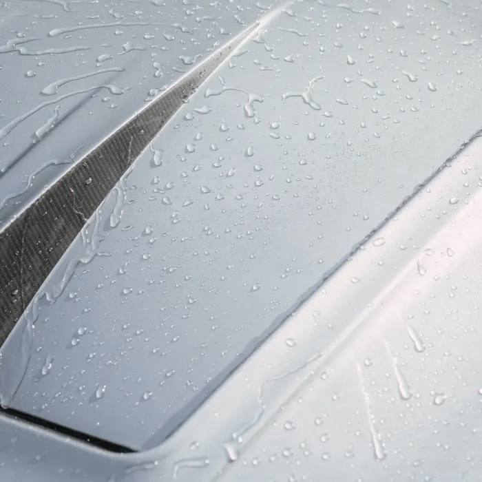 Raindrops cover a silver car hood featuring a sleek vent, suggesting recent rainfall.