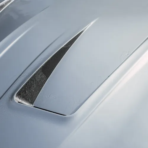 A close-up of a car hood featuring a sleek, integrated air vent; the surface shows slight traces of condensation, indicating a moist or recently rained-on environment.