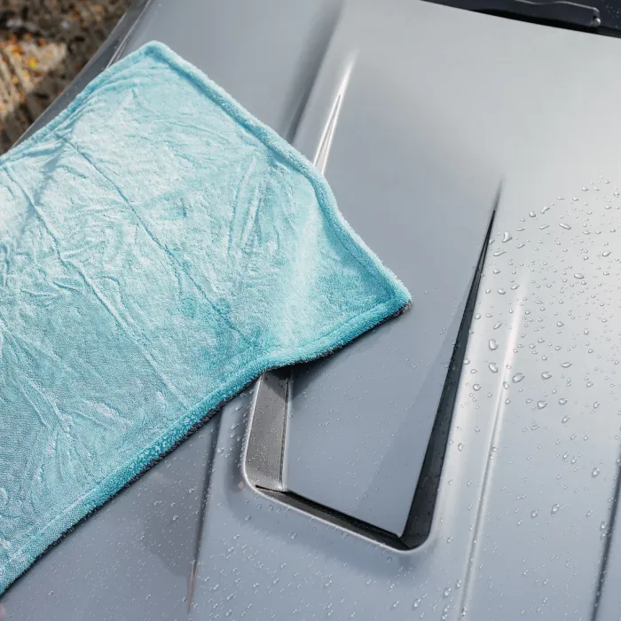 A light blue towel rests on the wet, glossy hood of a grey car, which is placed outdoors.
