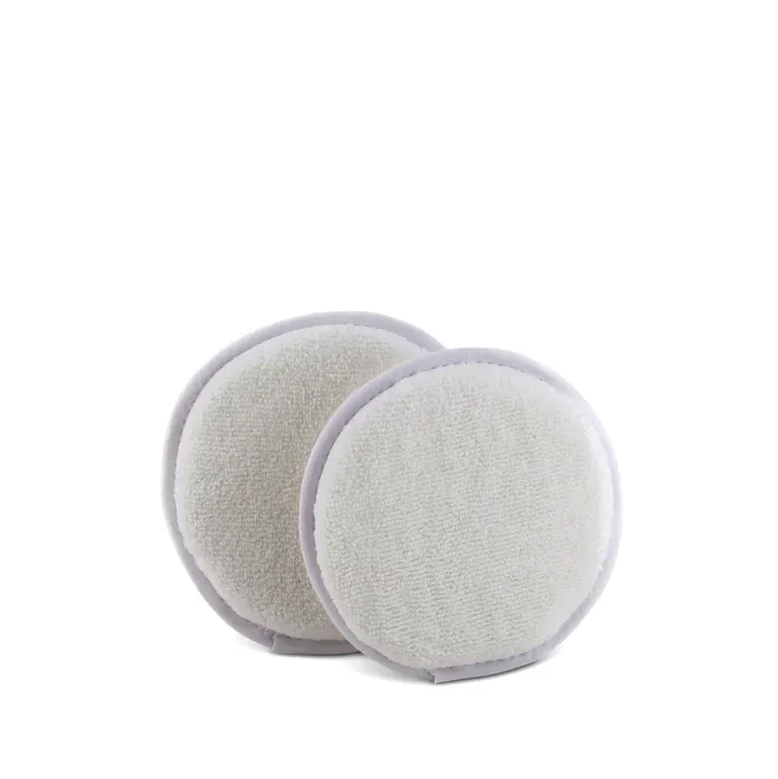 Two round, white reusable face pads with a soft, textured surface are stacked against a plain, white background. They have light gray borders.