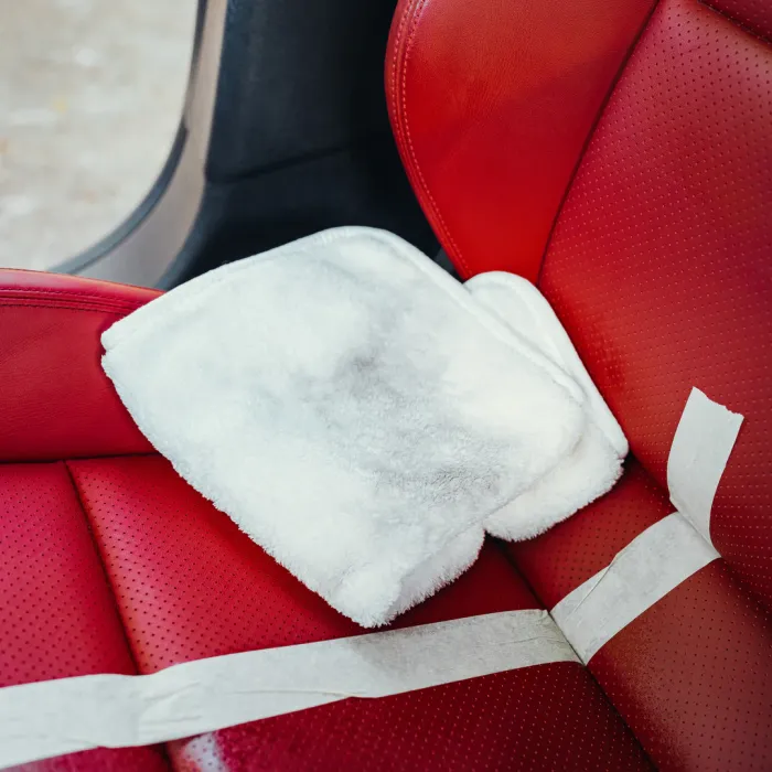 White cleaning cloths lie on a red car seat, with masking tape applied across the upholstery. A window is partially visible in the background.
