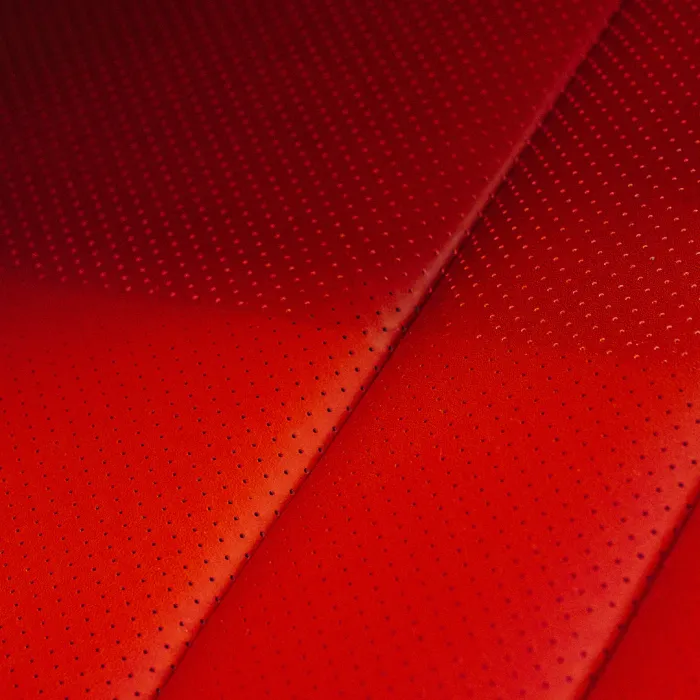 Red leather upholstery with evenly spaced perforations, shown in a close-up view. The perforated pattern varies in density across the surface.