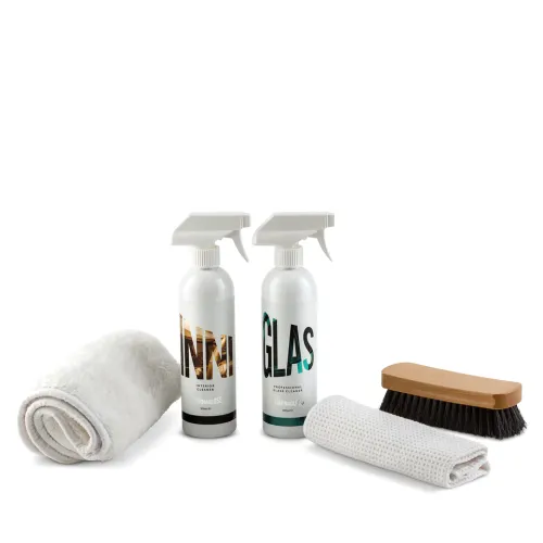 Two spray bottles labeled "INTERIOR CLEANER" and "GLASS CLEANER" stand beside a rolled white towel, a hand brush with black bristles, and a folded white cloth on a white background.