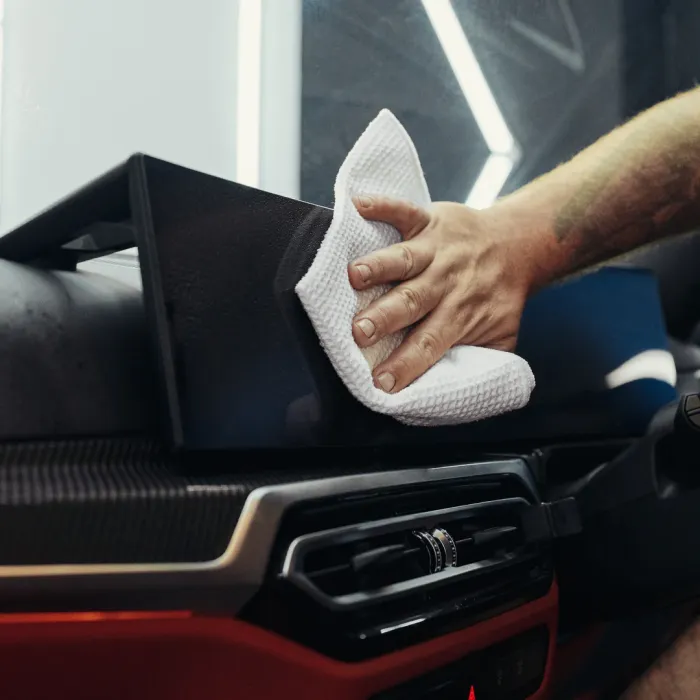 A hand holding a white cloth cleans the black dashboard of a car with a modern design.