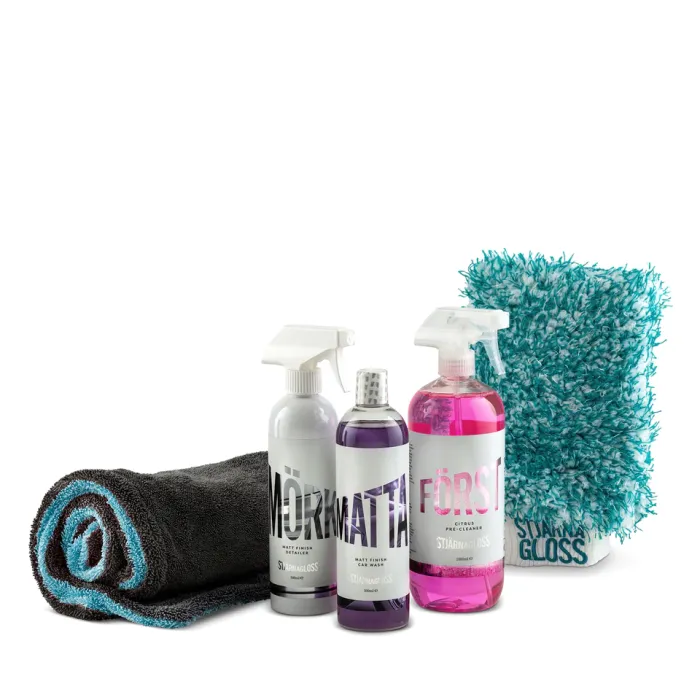 Cleaning products including a rolled-up black towel, two spray bottles labeled "Mörkmatta" and "Förseglare," one bottle labeled "Mattarengöring," and a blue and white microfiber mitt, all on a white background.