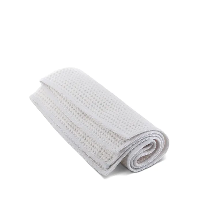 A white, folded, waffle-textured cloth lies on a plain white surface, neatly rolled at one end.