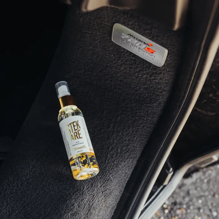 A bottle of Stekare Air Freshener lies on a black car floor mat beside a silver "McLaren MP4-12C Launch Edition 001/001" badge.