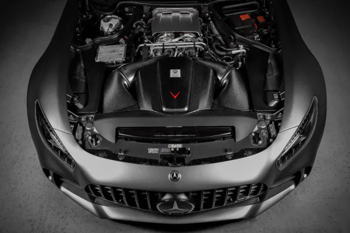 Engine compartment of a sleek, silver Mercedes-Benz sports car, displayed with an open hood in a dimly lit garage.