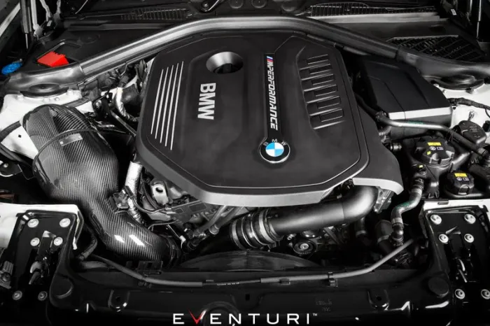 An engine labeled "BMW" and "M PERFORMANCE" is installed in a vehicle, with components including hoses and a carbon fiber air intake visible in a well-maintained engine bay. "EVENTURI" at the image bottom.