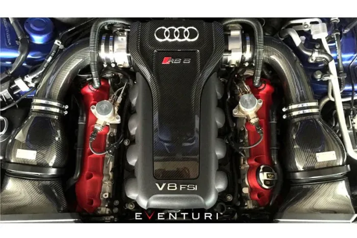 V8 engine with a carbon fiber cover, displaying the Audi logo, "RS5," and "V8 FSI" text, situated in a car engine bay with surrounding red and black components. Text at bottom says "EVENTURI."