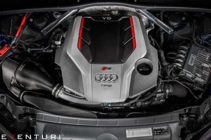 Audi V6 engine with red trim detailing, bearing logos for "Audi," "G S," and "TFSI." It is installed in a car engine bay, surrounded by various automotive components. Text: "EVENTURI."