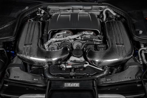 A car engine equipped with polished carbon-fiber intake manifolds, located in a dark engine bay with various metal and plastic components.