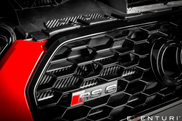 Grille with "RS6" badge on a red vehicle, focusing on the black hexagonal design, with "EVENTURI™" text in the corner. The background includes engine parts.