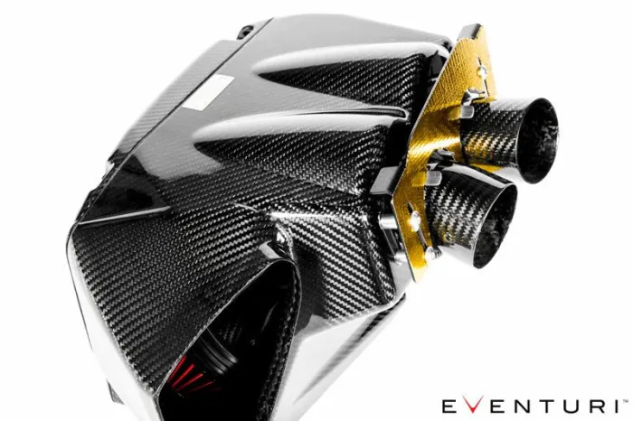 A carbon fiber engine air intake system with dual cylindrical filters is mounted on a metallic gold panel. Text reads "EVENTURI" at the bottom right. The context is a white background.