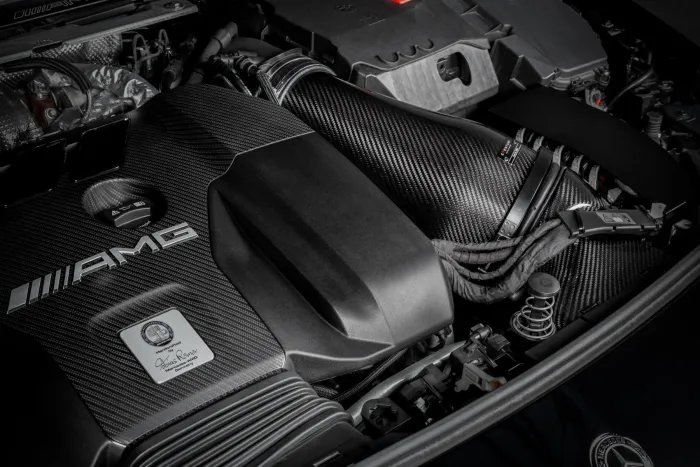 A carbon-fiber-clad AMG engine sits within a car’s engine bay. On it is a metallic emblem with the text, “Handcrafted by Tobias Rommel, Affalterbach, Germany,” highlighting its handcrafted nature.