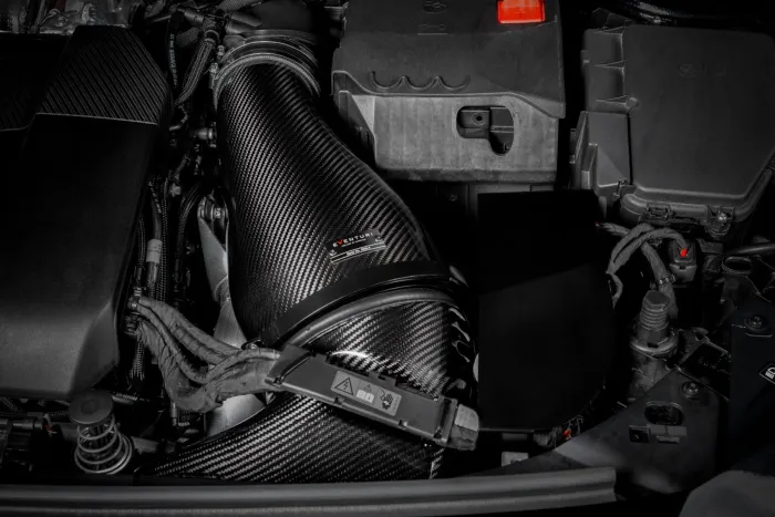 A carbon fiber air intake pipe, labeled "EVENTURI," is attached to an automobile's engine, surrounded by various engine components and wiring within the engine bay.