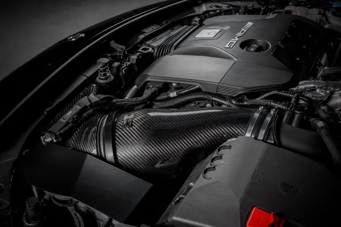 The image shows a high-performance car engine with "AMG" branding, featuring prominent carbon fiber components and intricate wiring, situated within a well-organized engine bay.