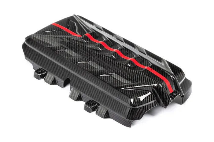 Black carbon fiber engine cover with a red, wavy stripe and intricate patterns, resting on a plain white background.
