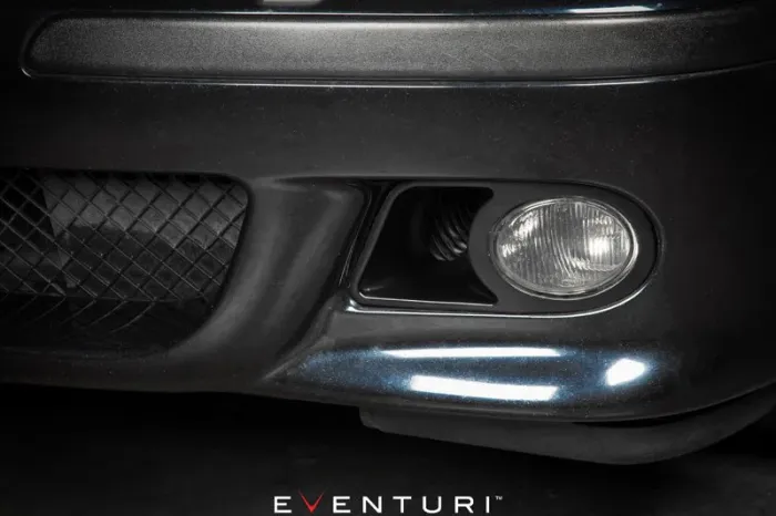 A close-up of a car's front bumper featuring a fog light on the left side next to a black mesh grill. Text: "EVENTURI" at the bottom.