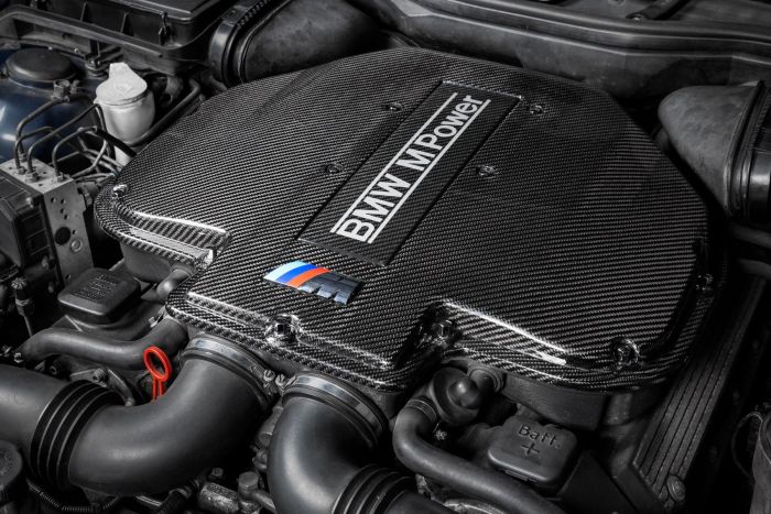 Carbon fiber engine cover labeled "BMW M Power" and featuring the BMW M logo, situated within an intricate car engine compartment.