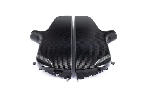 A carbon-fiber engine cover with a sleek, black finish, lies split into two sections, symmetrically aligned with various attachment points, set against a plain white background.