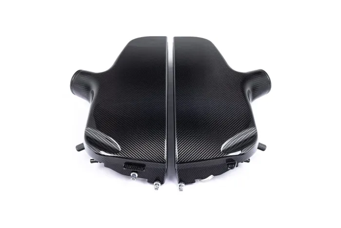 A carbon-fiber engine cover with a sleek, black finish, lies split into two sections, symmetrically aligned with various attachment points, set against a plain white background.