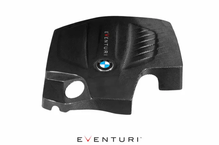 A carbon fiber BMW engine cover features the text "EVENTURI" vertically and the BMW logo centrally displayed. The background is plain white, highlighting the part's sleek design.