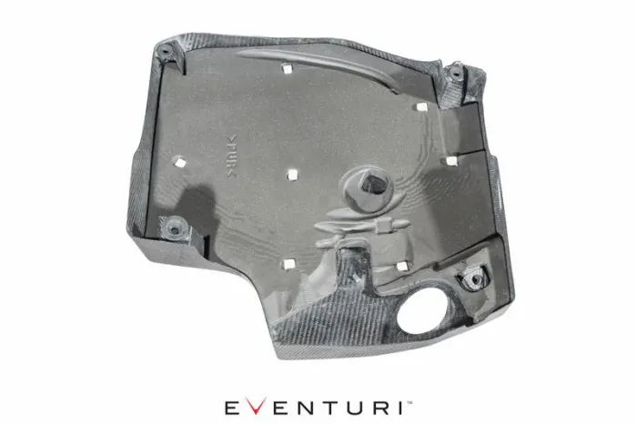 A carbon fiber engine cover with "EVNTURI" text at the bottom, featuring multiple cutouts and mounting points. The context is a clean white backdrop and "PUR" imprint on the cover.