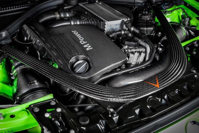 Carbon fiber-covered engine with “M Power” text displayed amidst various components and bright green accents in the surrounding car body, suggesting a high-performance vehicle.