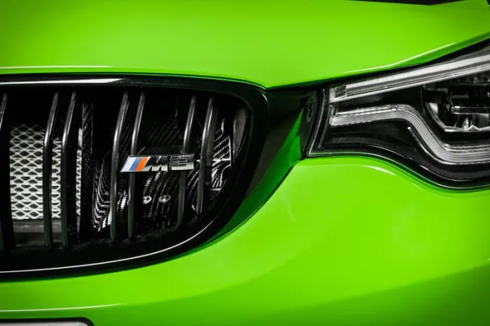 Close-up of a vibrant green car's front end; featuring a chrome grille with "M3" badge and sleek, modern headlight design against a black background.