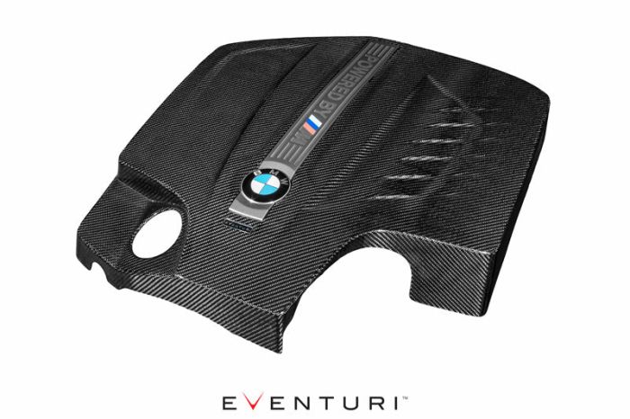 Carbon-fiber engine cover with BMW logo and M stripes inlay, resting isolated on white background. Text: "POWERED BY M" and "EVENTURI" at the bottom.
