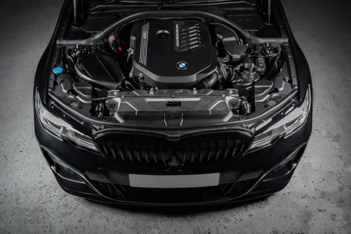 Engine of a BMW car with an open hood showcasing a clean and organized engine bay in a dimly lit garage with a concrete floor.