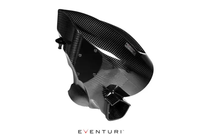 Carbon fiber intake manifold displayed against a white background; it's sleek, angular, with visible screws and mounting points. Eventuri logo present at the bottom center.