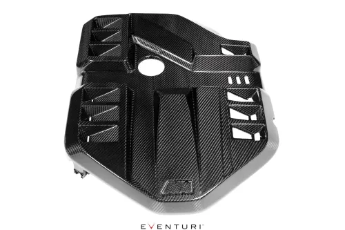 A carbon fiber engine cover with multiple geometric vents and a circular opening in its center, positioned on a white surface. Text: "EVENTURI."