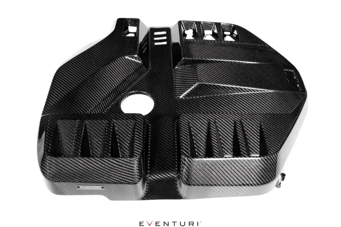 Rectangular, glossy carbon fiber vehicle engine cover with various geometric patterns and vents, and a central circular hole, placed against a white background. Text present: "EVENTURI".