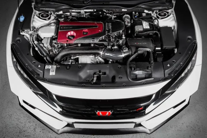 Car engine bay with a red intake cover, labeled "CETUS," and carbon fiber components. Context is a white sports car with its hood open in a brightly lit garage.